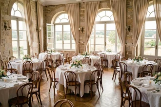 Salle de réception élégante dans le Rhône avec tables rondes dressées et fenêtres en arche